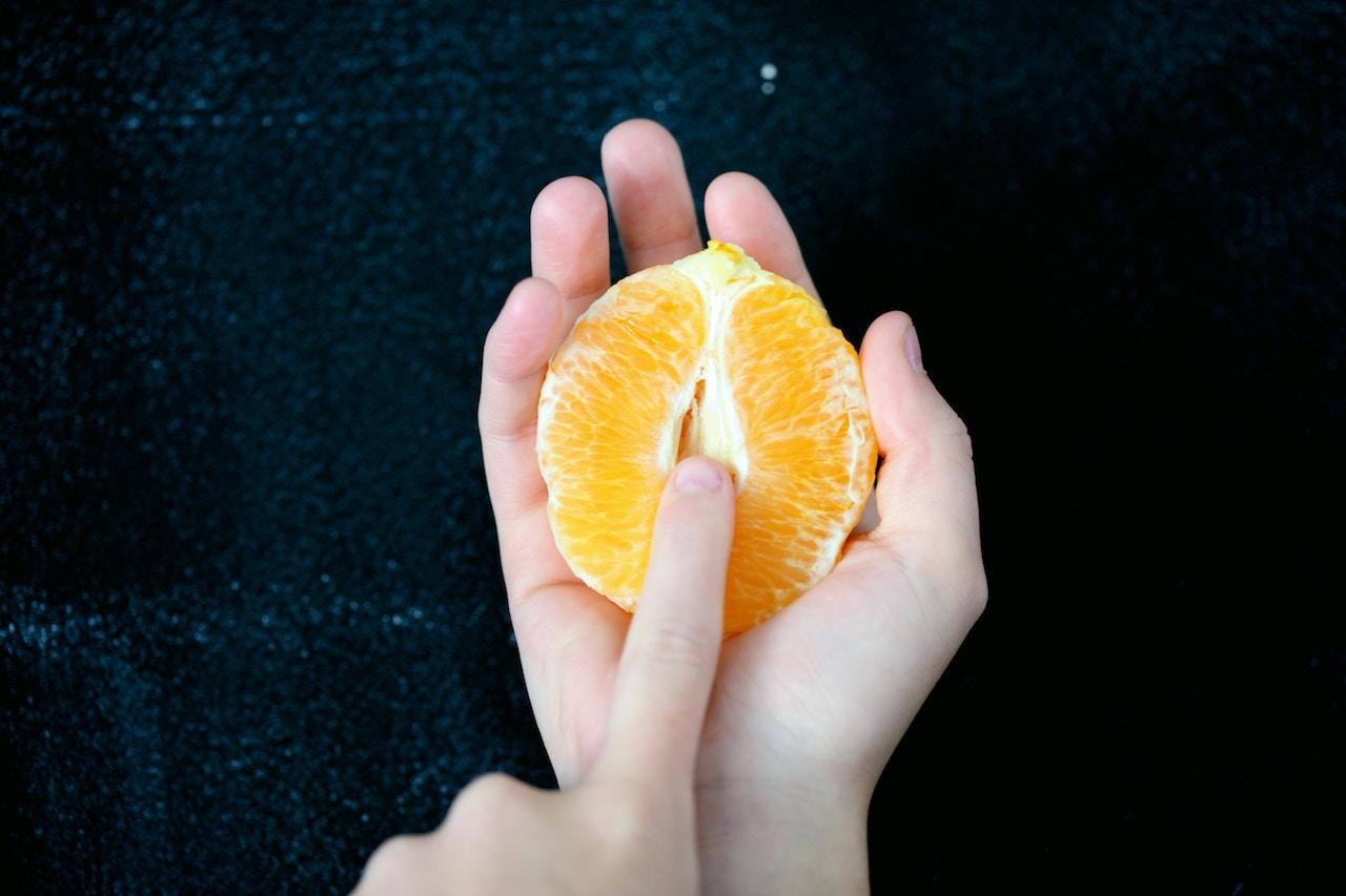 Käsiä pitelemässäs halkaistua appelsiinia, osoittaen keskelle sormella